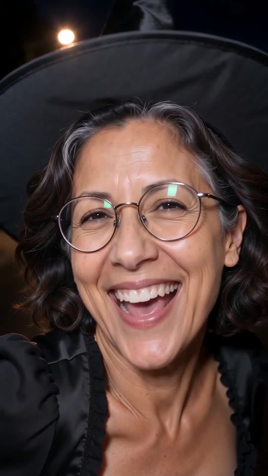 Still from a video made on this site: a close-up of a smiling woman in a witch hat